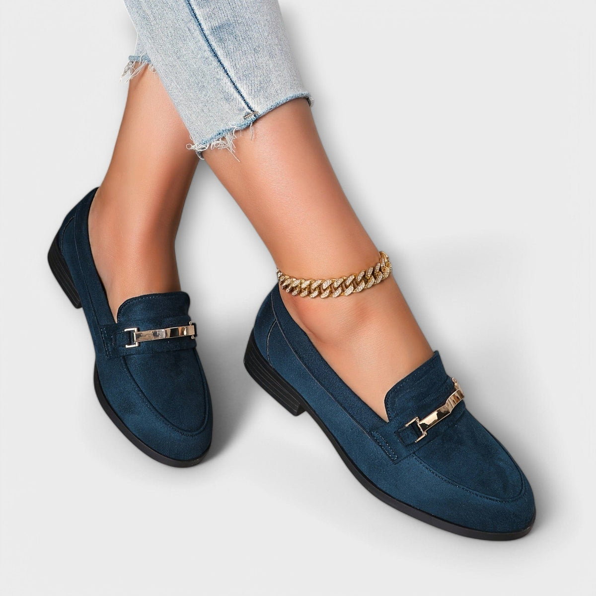 Navy suede loafers with gold buckle detail and short metal chain bracelet-style charm