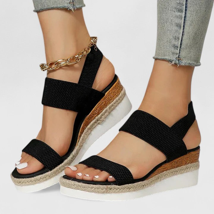 Black orthopedic sandals with wide straps, espadrille sole, and gold chain ankle strap