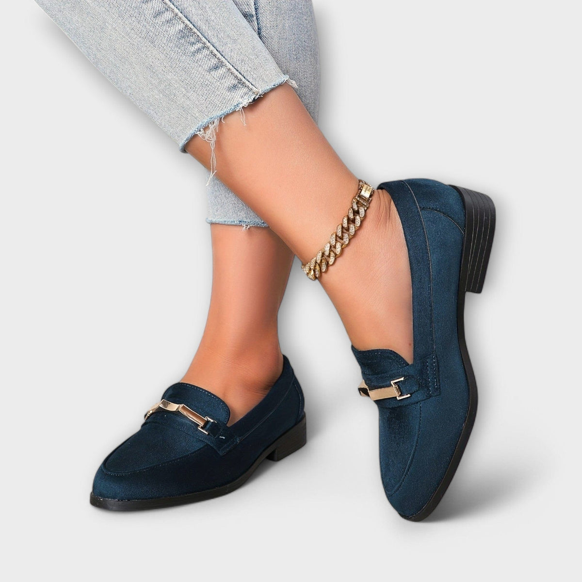 Navy low heel loafers with gold buckle strap detail and chain bracelet at ankle
