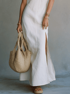 White maxi dress lower half with side slit, woven tote and flat sandal shoes