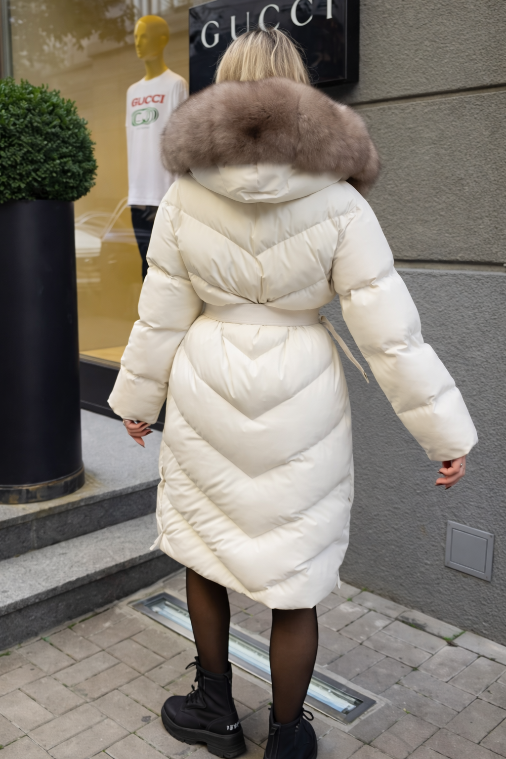 White long puffer coat with taupe fur hood and waist tie belt, back view.
