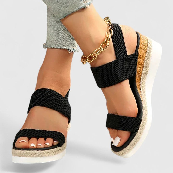 Black orthopedic sandals with wide straps, tan espadrille sole, and gold chain ankle strap