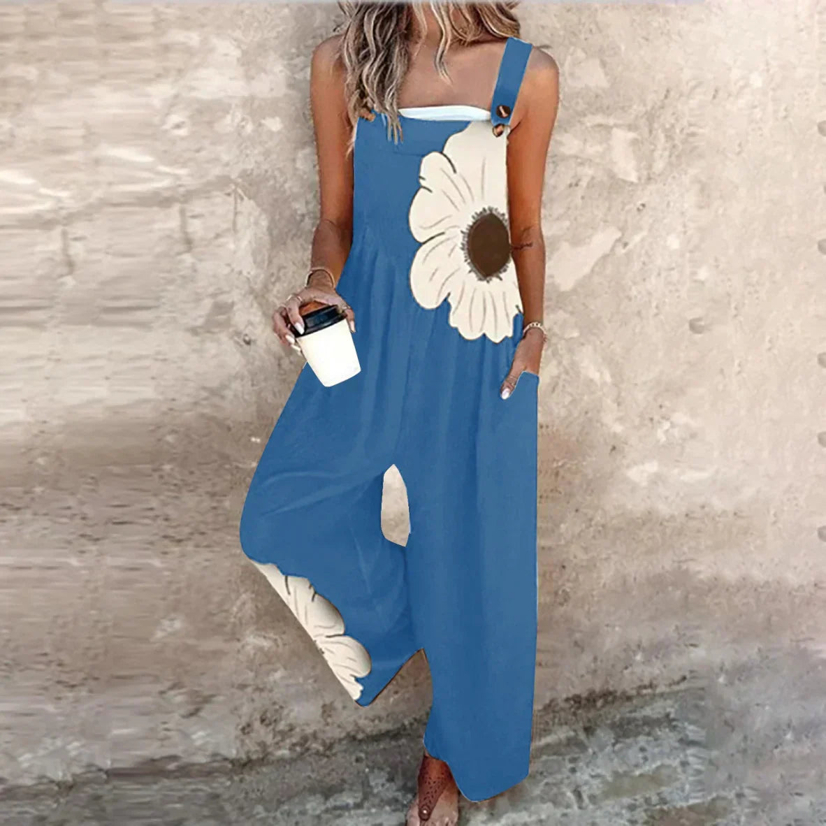 Blue sleeveless jumpsuit with white daisy print, wide legs, and button-accent strap