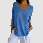 Blue knit v-neck top with three-quarter sleeves and a loose draped silhouette.