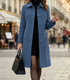 Blue long coat with notched lapels and button front, worn over a dark dress