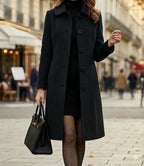 Black long coat with notched lapels and button closure, worn over a dark outfit