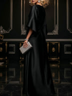Black satin maxi dress with loose cape sleeves and side draped skirt
