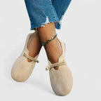 Beige suede slip-on loafers with braided tie strap, worn with ankle bracelet