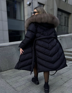 Black long puffer coat with taupe fur hood and gathered waist tie from back view.