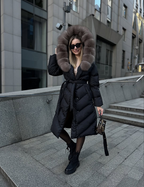 Black long puffer jacket with large taupe fur hood and tie waist detail.