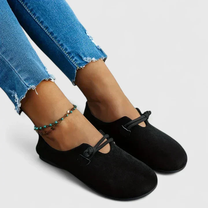 Black suede slip-on loafers with top tie strap, worn with ankle bracelet