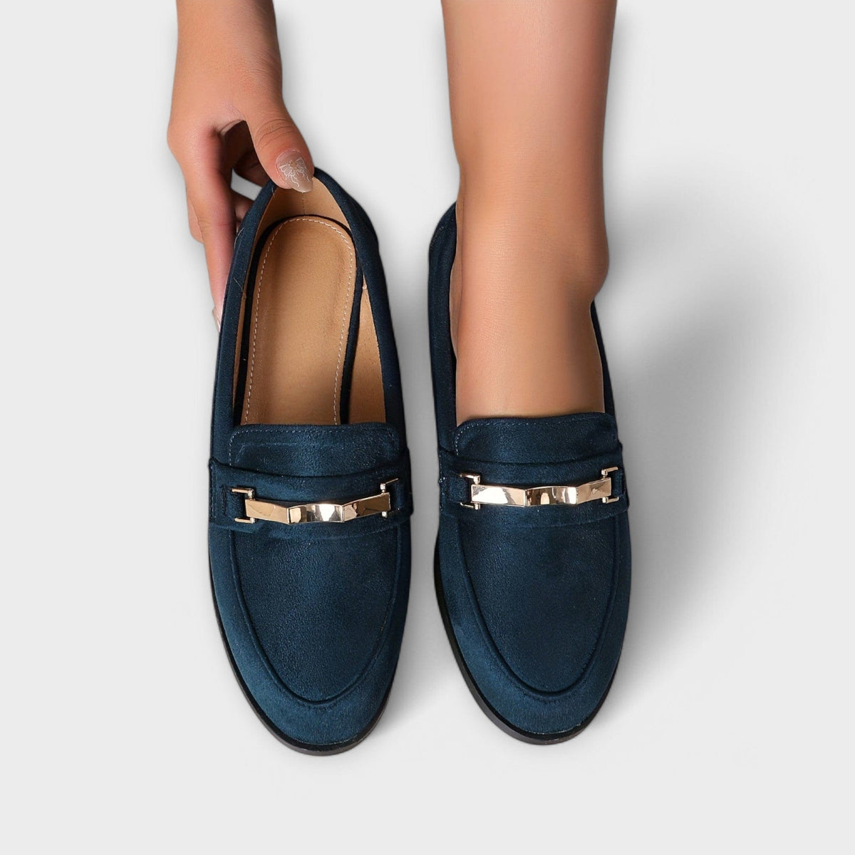 Navy suede loafers with gold buckle strap detail, showing inner lining and toe shape