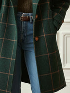 Dark green plaid tweed coat hem with front buttons over blue jeans