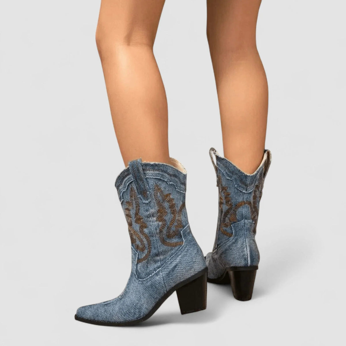 Blue denim ankle boots with brown embroidered swirl, slight back angle